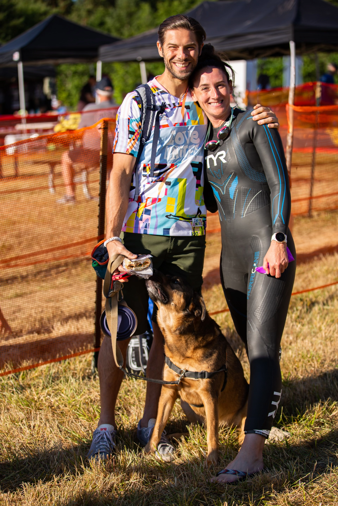 man dressed casually and woman wearing a wetsuit with a dog between them
